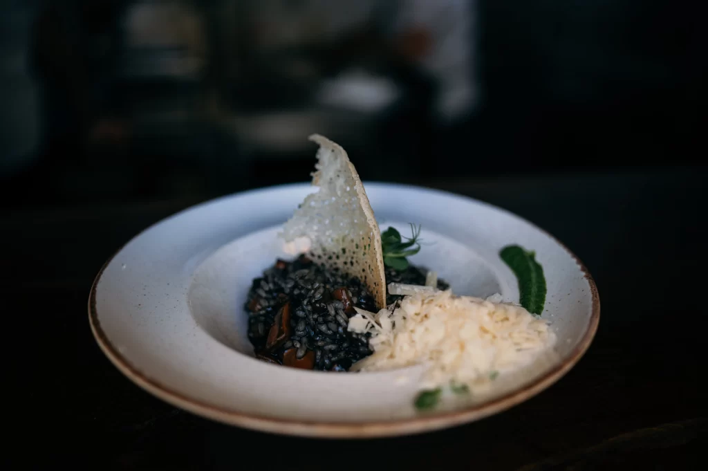 Black risotto with cuttlefish ink, grated cheese, and crisp parmesan garnish served at Konoba Malo Misto restaurant in Zadar
