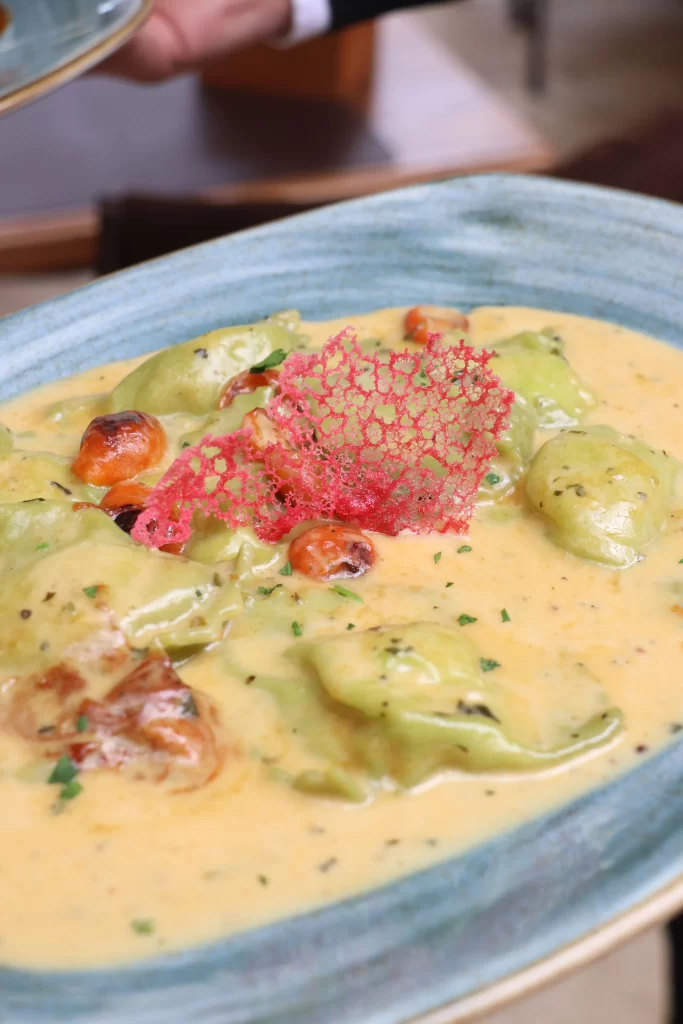 Homemade green ravioli filled with seafood in a creamy saffron sauce, topped with red lace garnish and cherry tomatoes, served at Konoba Malo Misto