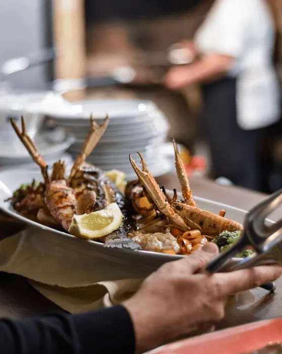 Waiter serving a platter of grilled langoustines, prawns, and fish with lemon wedges at Konoba Malo Misto restaurant in Zadar
